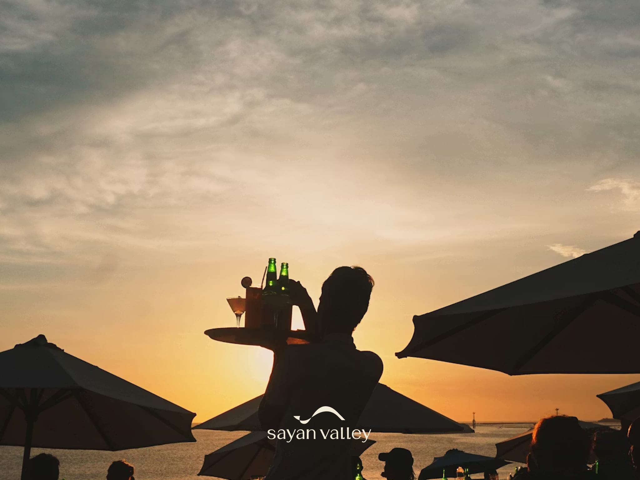 Silhouette of a waiter serving drinks at a beach club during the peak bali sunset time.
