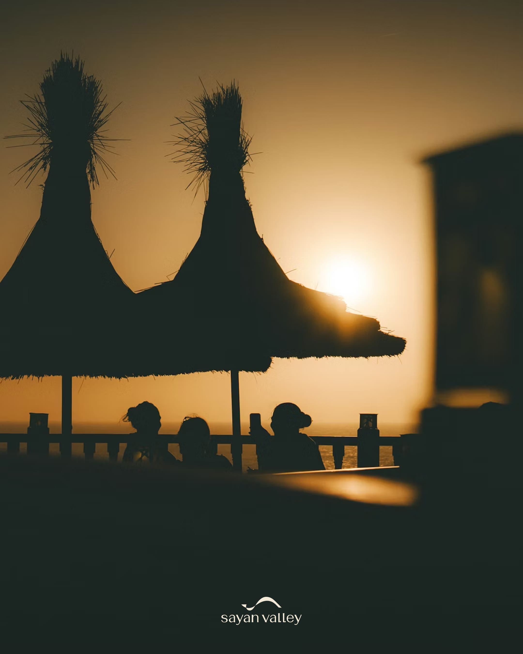 Silhouetted guests relaxing under thatched umbrellas during the golden sunset in bali time.